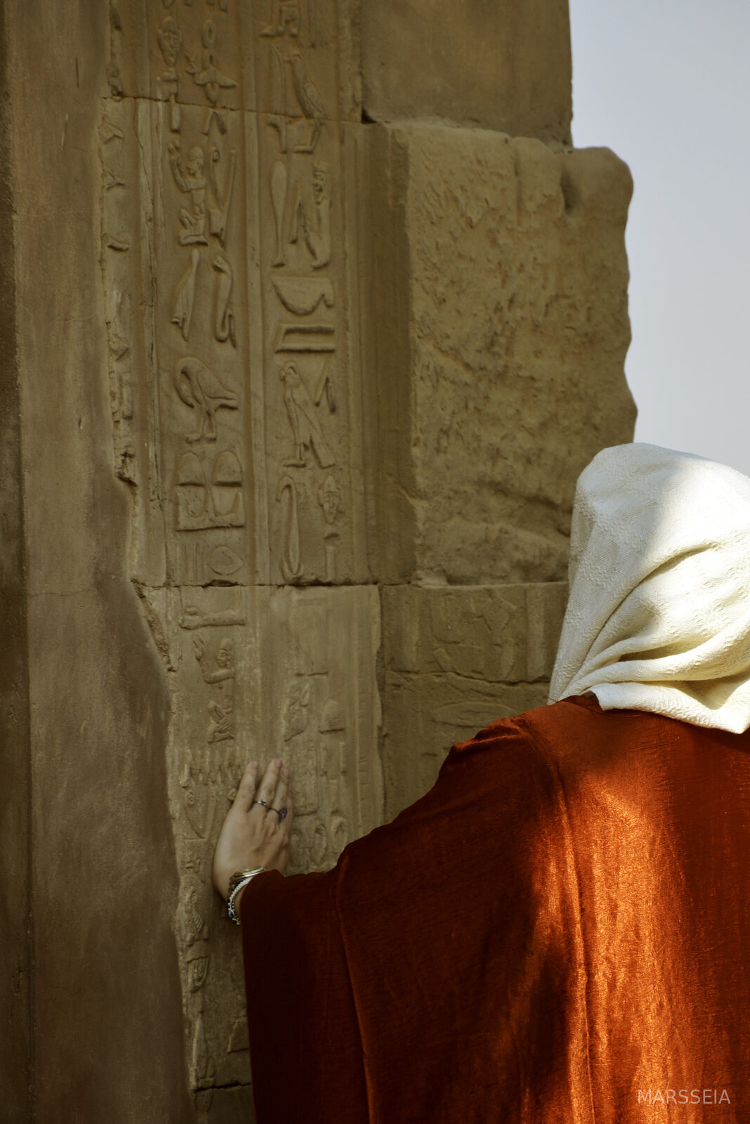 A woman in a red and white veil touching a temple wall, Egypt