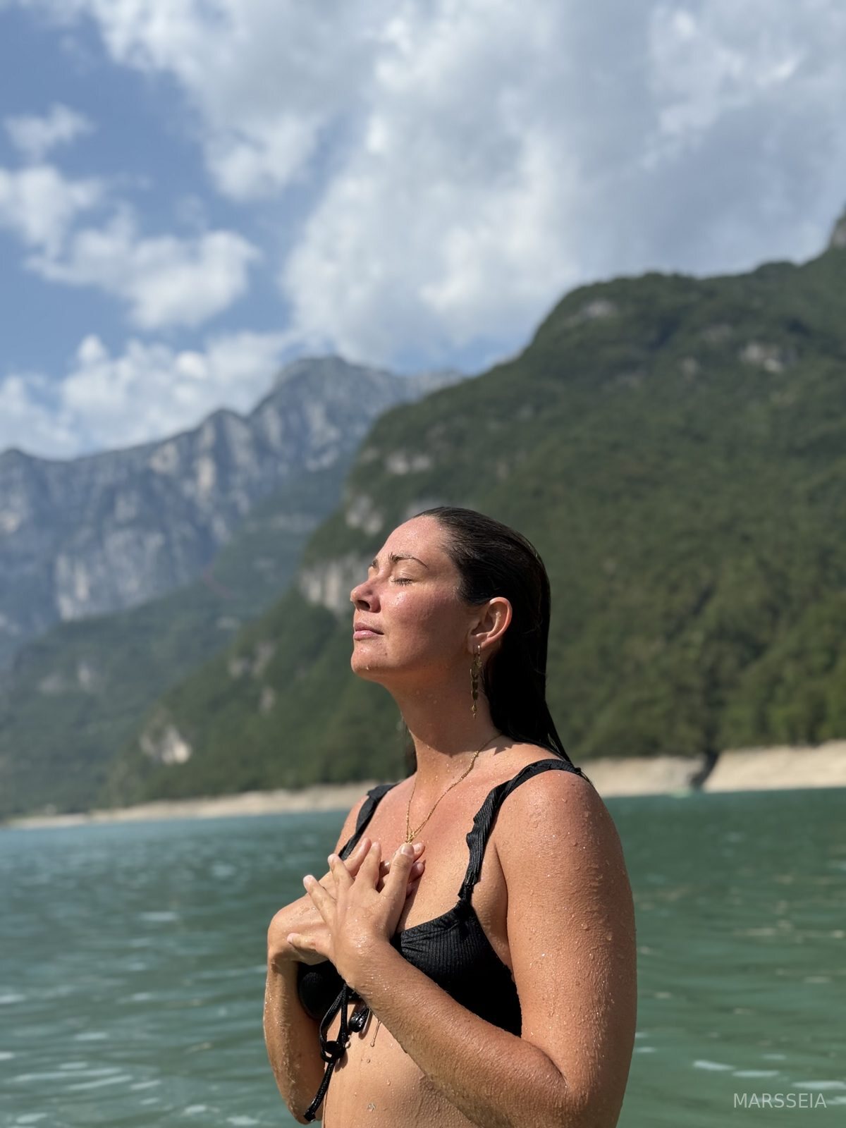 A woman in a mountain lake with her hand on her heart, Dolomites